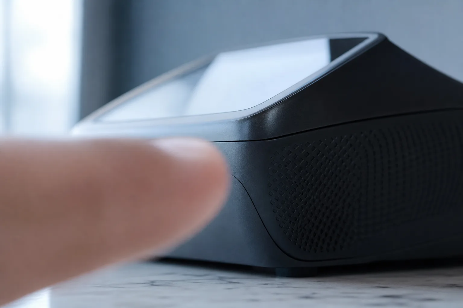 Close-up of a contactless payment terminal on a café counter, with a blurred fingertip in the foreground.